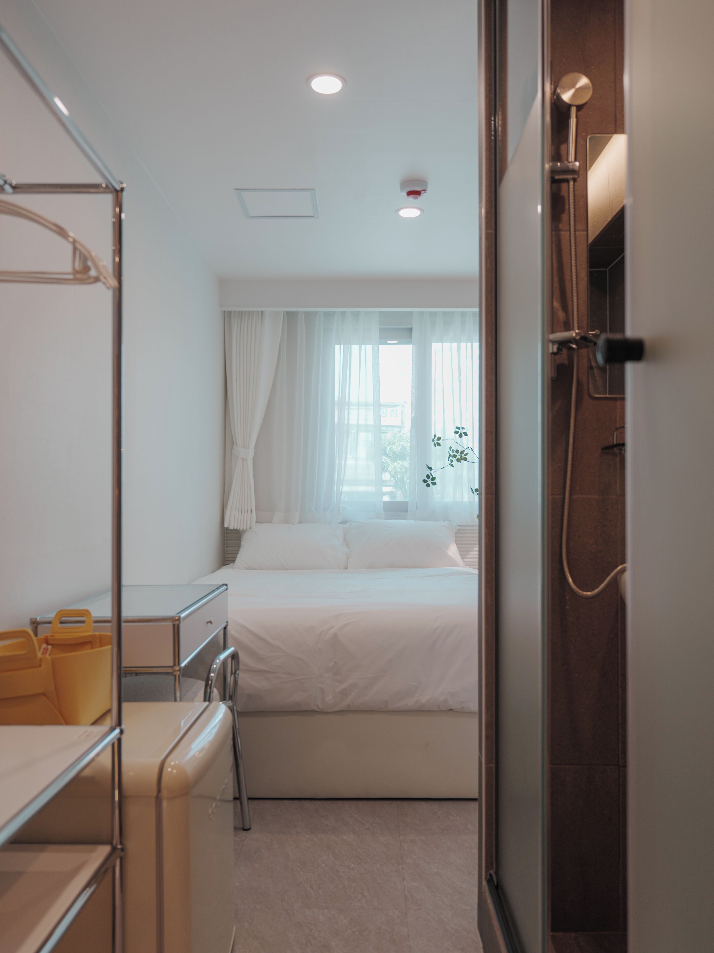 A hotel room with a bed, a bedside table, a chair, a wardrobe, and a shower area.