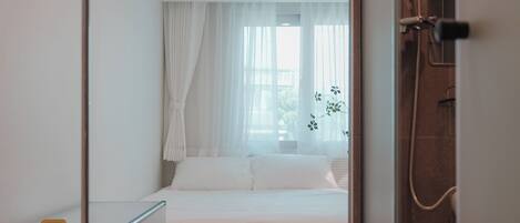 A hotel room with a bed, a bedside table, a chair, a wardrobe, and a shower area.