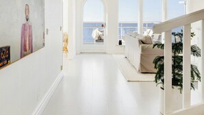 A spacious interior with a high ceiling, a large painting on the wall, a staircase leading to an outdoor area, and a view of the sea through large windows. - Modern villa with sea views in picturesque Mölle (Mölle)