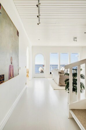 A spacious interior with a high ceiling, a large painting on the wall, a staircase leading to an outdoor area, and a view of the sea through large windows. - Modern villa with sea views in picturesque Mölle (Mölle)