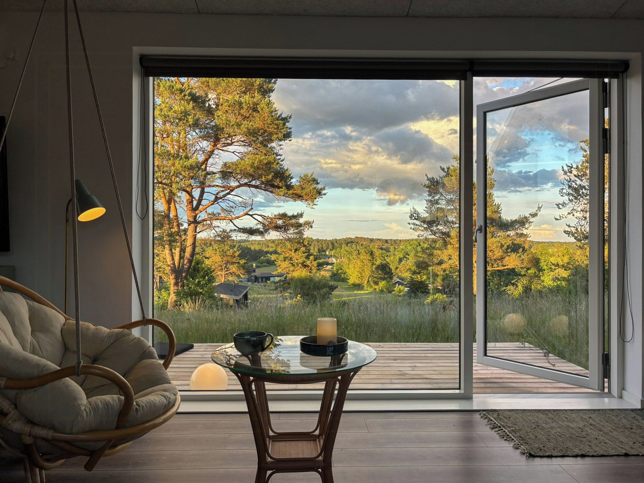 Un intérieur moderne avec une grande porte vitrée donnant sur une terrasse offrant une vue sur un paysage boisé.