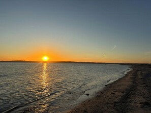Platja al capvespre amb el sol reflectint a l'aigua.