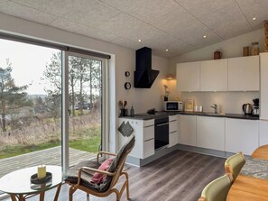 Une cuisine moderne dotée d’une grande fenêtre, un coin repas avec une table en verre et un espace salon confortable.