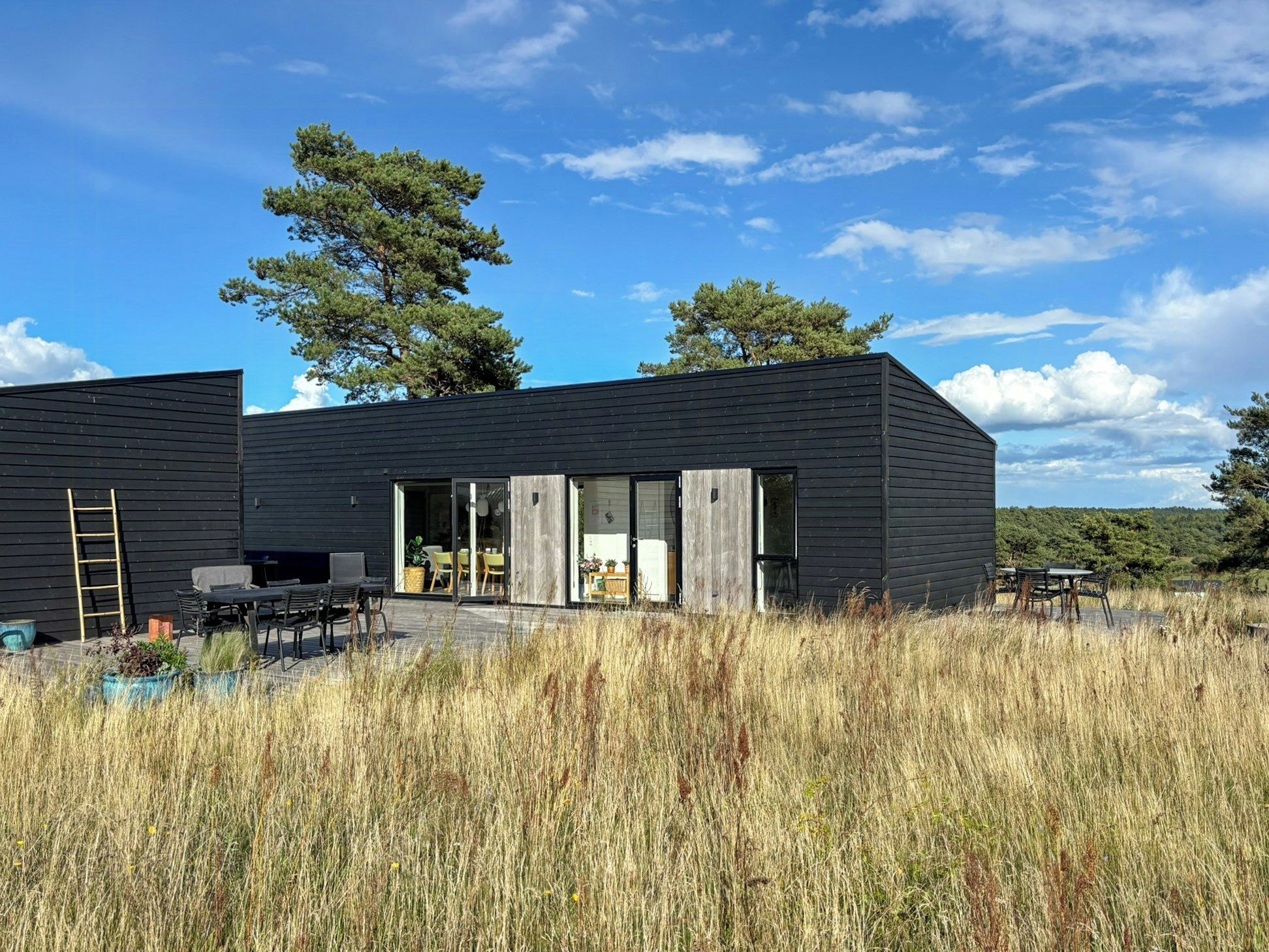A modern black building with a patio area, outdoor seating, and a ladder.