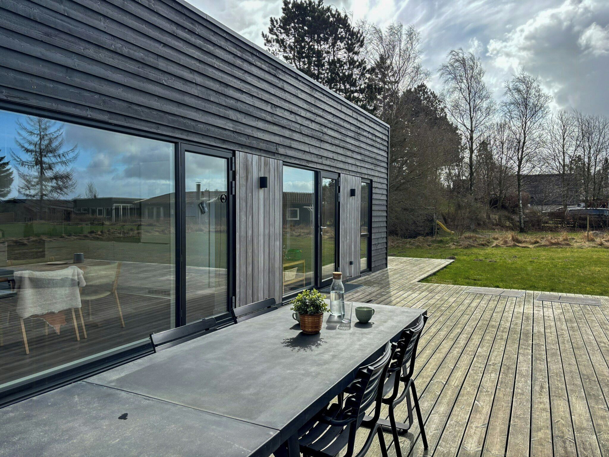 Una casa moderna con amplios ventanales, una terraza y mobiliario exterior.