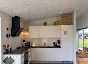 A modern kitchen with white cabinets, a microwave, a kettle, and a basket on the counter. - Holiday home in protected nature near Mols Bjerge (Ebeltoft)