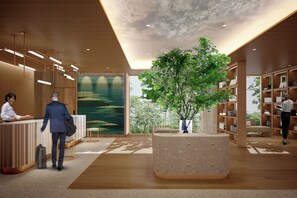 Um saguão de hotel moderno com piso de madeira, balcão de recepção, uma grande planta em vaso e uma estante repleta de livros.
