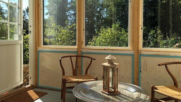 A room with a glass table, two wooden chairs, a lantern, and a view of trees through large windows. - Artist studio by Helge River in Skåne (Broby)