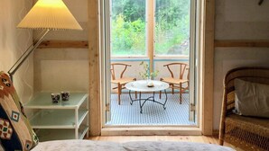 A cozy room with a bed, a table with chairs, a lamp, and a view of greenery through a window. - Artist studio by Helge River in Skåne (Broby)