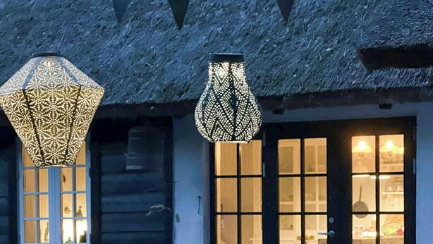 Een landelijk gebouw met rieten dak, grote ramen en hangende decoratieve verlichting.