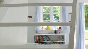Una habitación con techo y barandal blancos, y una ventana con cortinas.
