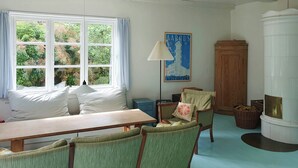 Una habitación con un ventanal grande, una mesa, dos sillas, una lámpara, un armario y una chimenea.