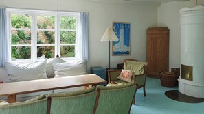 Ein Zimmer mit großem Fenster, einem Tisch, zwei Stühlen, einer Lampe, einem Schrank und einem Kamin.