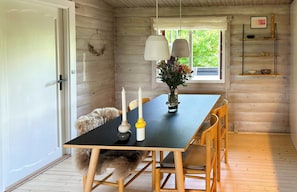 A wooden interior with a dining table, chairs, a vase with flowers, and a window with a view. - Log cabin in the front row overlooking the sea (Tranekær)