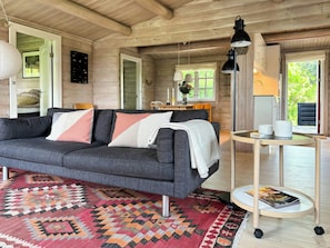 A cozy living room with a sofa, patterned rug, and a small table with magazines. - Log cabin in the front row overlooking the sea (Tranekær)