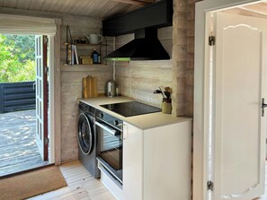 A compact kitchen with a built-in washer, a stove, and a black range hood. - Log cabin in the front row overlooking the sea (Tranekær)