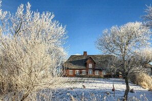 Ein Haus mit Strohdach, umgeben von schneebedecktem Gelände und kahl stehenden Bäumen.