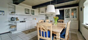 A modern kitchen with white cabinetry, a wooden dining table, and pendant lights. - Thatched house on a Warft near Schlüttsiel (Dagebüll)