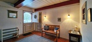 A room with a wooden bench, a small table with a lamp, a mirror, and a door with a wreath. - Thatched house on a Warft near Schlüttsiel (Dagebüll)
