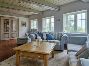 A living room with a wooden coffee table, striped sofas, and a view through large windows. - Thatched house on a Warft near Schlüttsiel (Dagebüll)