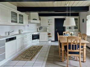 Eine moderne Küche mit weißen Schränken, einem eingebauten Ofen und einem Essbereich mit einem Holztisch und Stühlen.