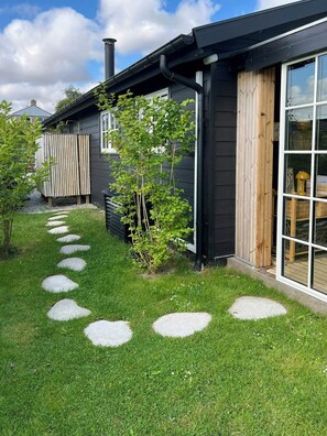A modern house with a black exterior, a wooden fence, and a stone pathway leading to the entrance. - Summer house by Nordstranden in Kerteminde (Kerteminde)