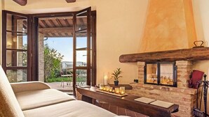 Um quarto acolhedor com sofá, uma mesa com velas, lareira e vista através de uma porta de vidro.