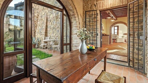 Um interior rústico com paredes de pedra, uma mesa de madeira e vista para o pátio externo.