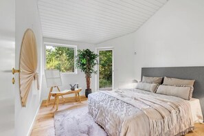 Ein Schlafzimmer mit einem Bett, einem Schreibtisch, einem Sessel, einer Topfpflanze und Blick auf Grün.