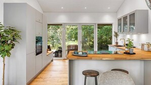 Una cocina moderna con encimera de madera, electrodomésticos integrados y grandes ventanales con vistas al verdor.