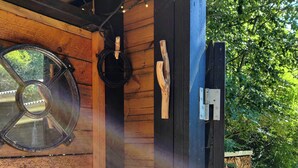 A wooden cabin with a large circular window, a black door, and a wooden post with a hook. - Home near beach with wilderness bath (Hurup Thy)
