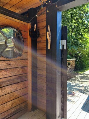 Eine Holzhütte mit einem großen Rundfenster, einer schwarzen Tür und einem Holzpfosten mit einem Haken.