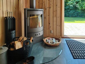 Ein Kaminofen, ein Glastisch, ein Korbkörbchen mit Steinen und ein Holzterrasse, die durch eine Glastür sichtbar ist.