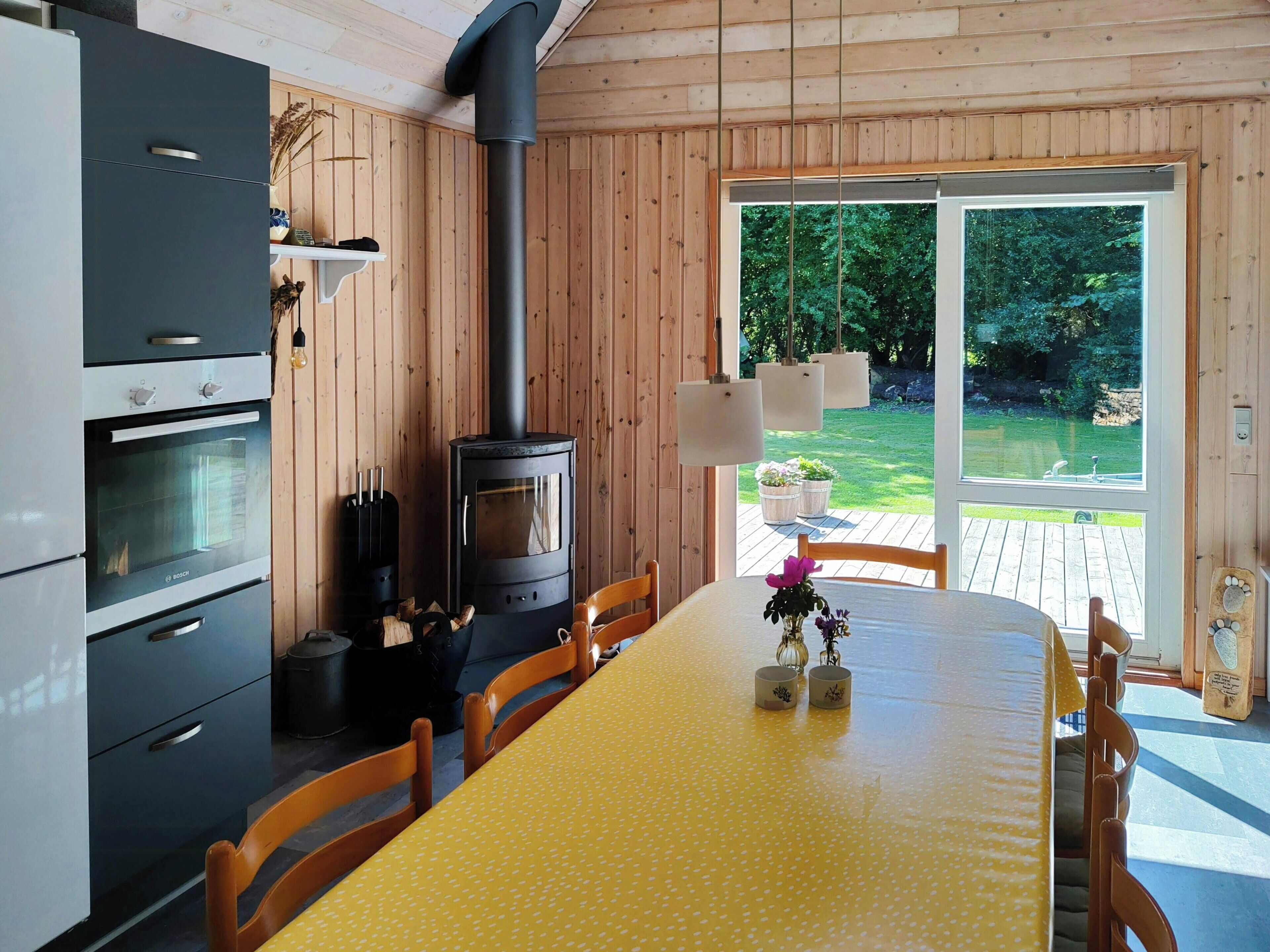 A modern kitchen with a built-in stove, oven, and cabinets, a dining table with chairs, and a view of a garden through a glass door.