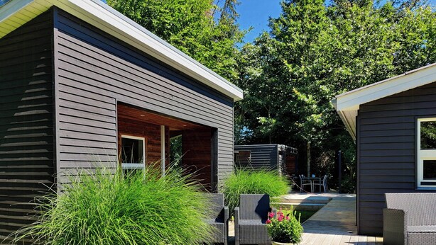 A modern house with a deck, a small outdoor seating area, and a large window. - Home near beach with wilderness bath (Hurup Thy)