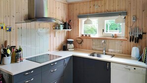 A modern kitchen with wooden paneling, a stainless steel sink, a dishwasher, and a window with a view of greenery. - Home near beach with wilderness bath (Hurup Thy)