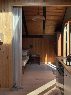 A cozy wooden cabin with a bed, a small table, and a kitchenette. - Modern 80s holiday home with a wild garden (Fårevejle)