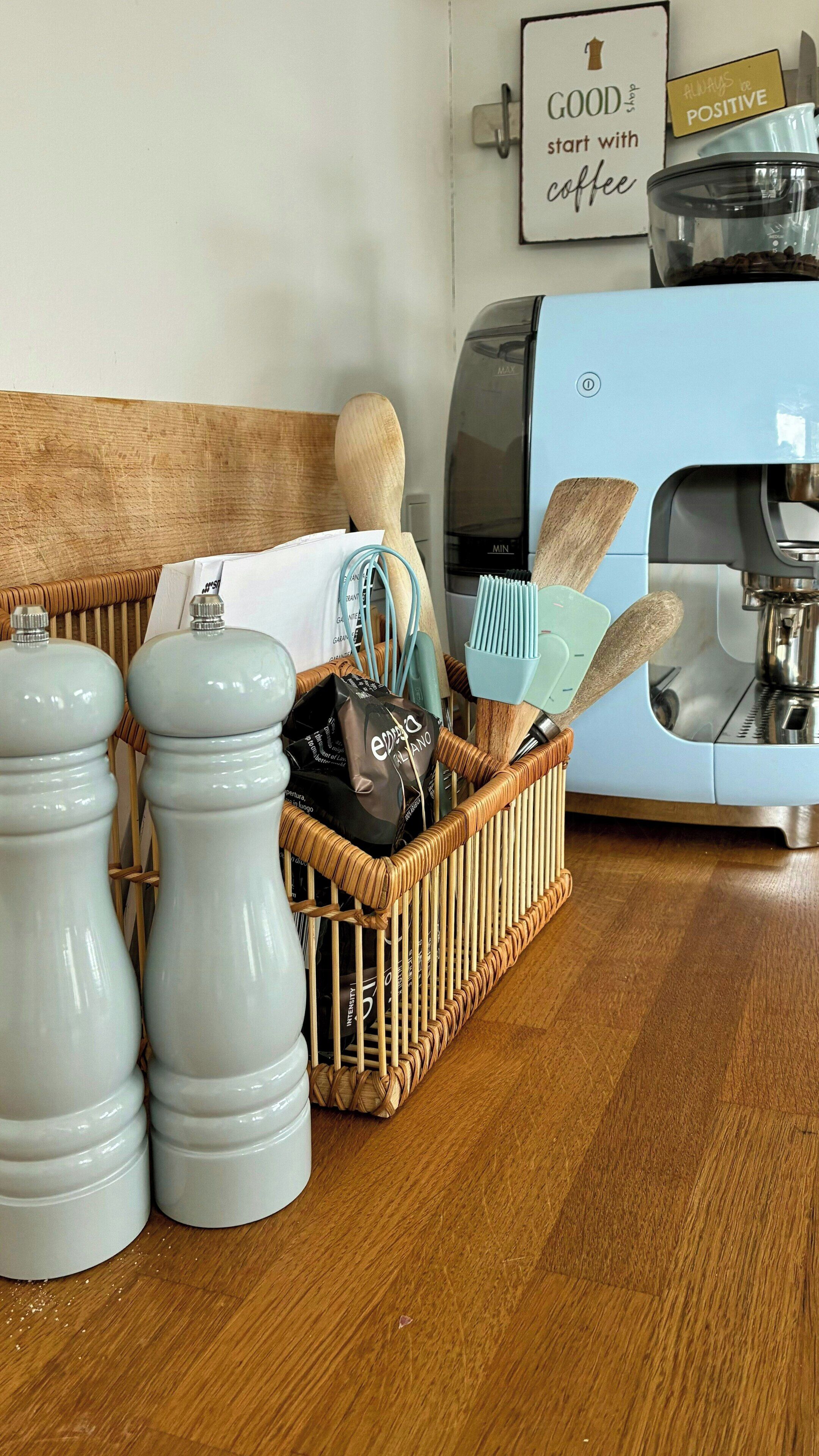 A kitchen area with a coffee machine, salt and pepper shakers, a wicker basket with kitchen utensils, and a sign on the wall.