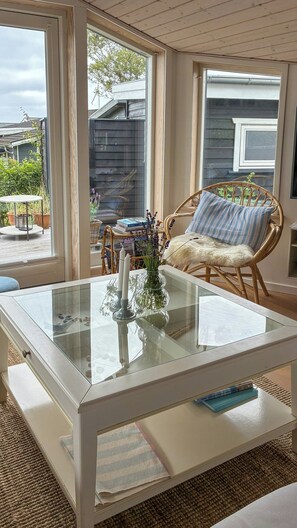 Quarto com mesa de vidro, cadeira de vime e vista para o exterior.