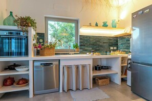 Eine moderne Küche mit Einbauofen, Geschirrspüler und Kühlschrank. Ein Fenster bietet Blick auf Bäume, und die Küche hat eine Wandverkleidung aus Ziegelsteinen.