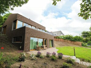 A modern two-story house with large windows, a patio with outdoor furniture, and a well-maintained garden. - Riverside architect-designed garden apartment (Stapel)