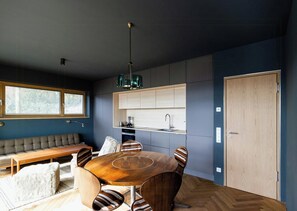 A modern kitchen with a built-in oven, a dining table with chairs, and a bench. - Riverside architect-designed garden apartment (Stapel)