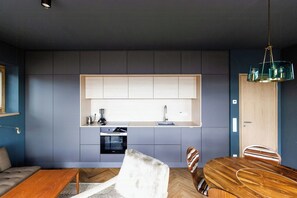 A modern kitchen with built-in appliances, a dining area with a wooden table and chairs, and a sofa. - Riverside architect-designed garden apartment (Stapel)