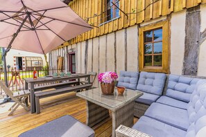 An outdoor seating area with a wooden deck, a glass-top table, a bench, a sofa, and a large umbrella. - Traditional house in the Gascogne forest (Trensacq)