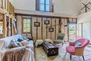 A rustic room with exposed wooden beams, a sofa, a chair, and a table with a suitcase. - Traditional house in the Gascogne forest (Trensacq)