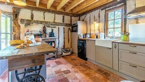 A rustic kitchen with exposed beams, a wooden table, and a vintage suitcase. - Traditional house in the Gascogne forest (Trensacq)