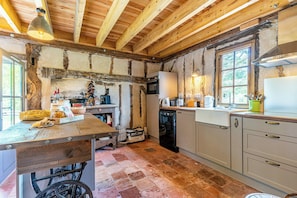 A rustic kitchen with exposed beams, a wooden table, and a vintage suitcase. - Traditional house in the Gascogne forest (Trensacq)