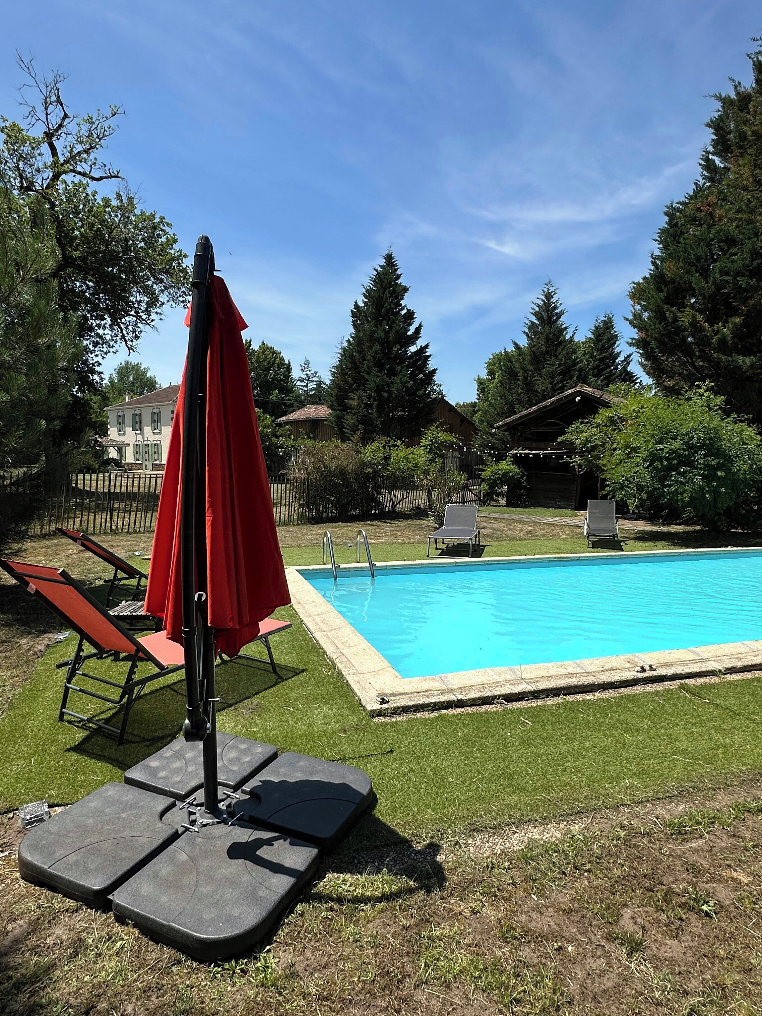 A swimming pool with a red umbrella, lounge chairs, and a wooden deck.