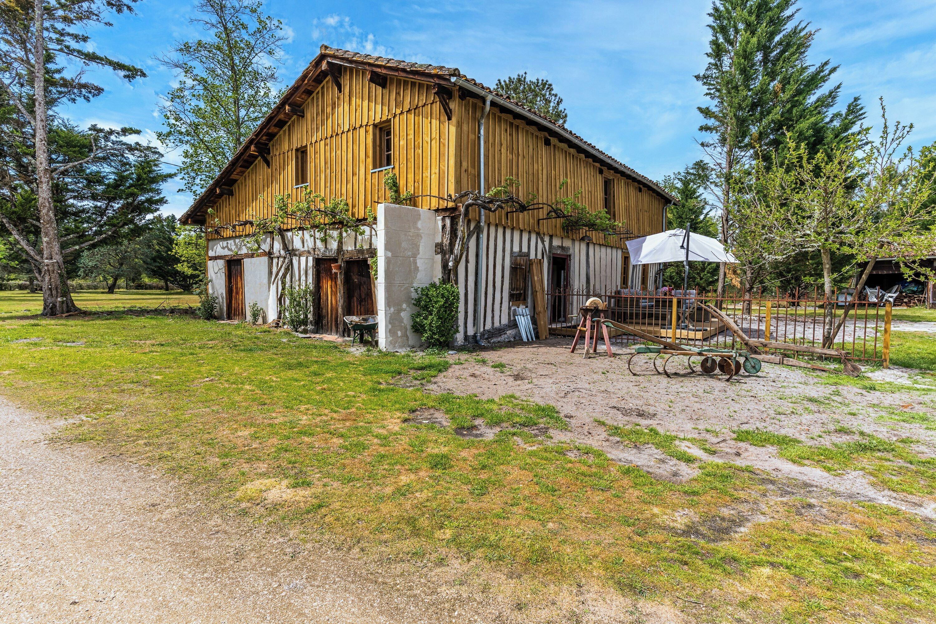 A rustic wooden building with a dirt yard, a swing set, and a covered area.
