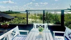 Una terraza con sillas blancas y una mesa, con vistas a un paisaje con vegetación y un edificio a la distancia.